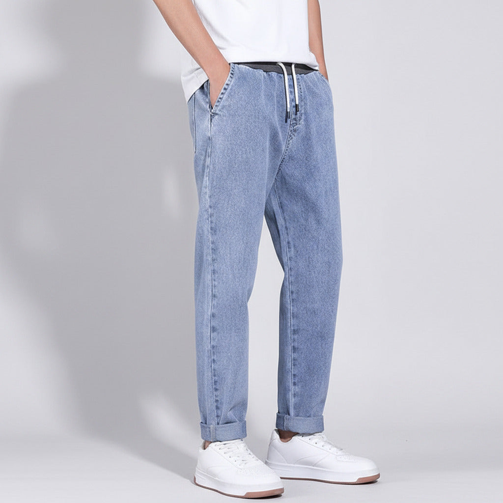 Person wearing light blue jeans and white sneakers on a gray background