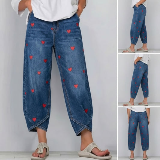 Blue jeans with red heart patterns worn by a person on a plain background